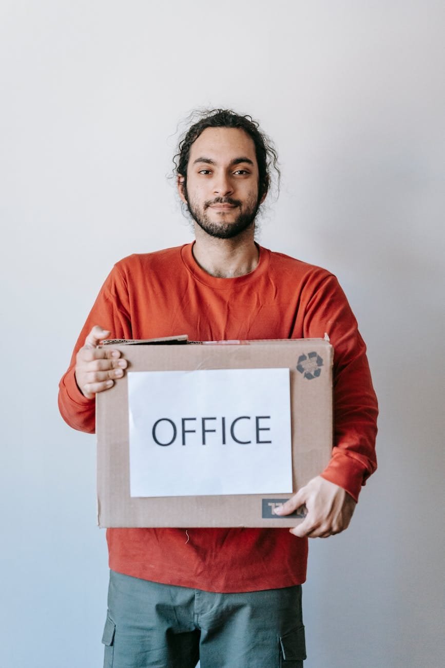 Smiling man holding a brown moving box with an OFFICE label