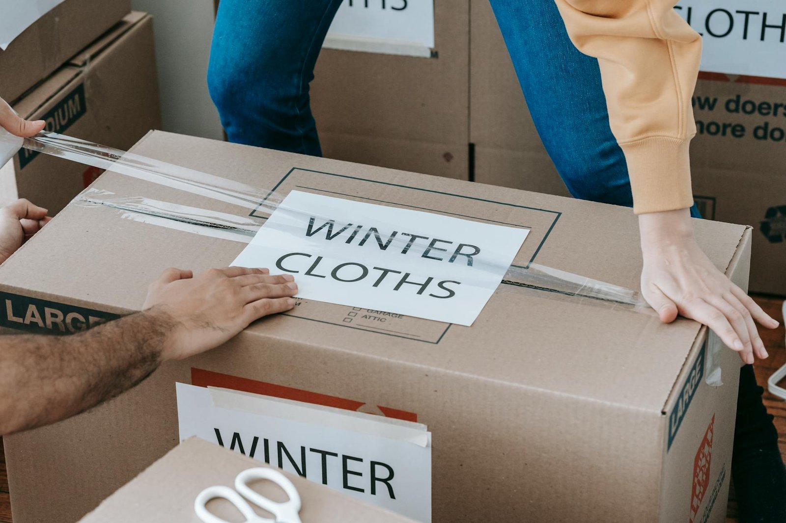 Two people taping a cardboard moving box labeled WINTER CLOTHS