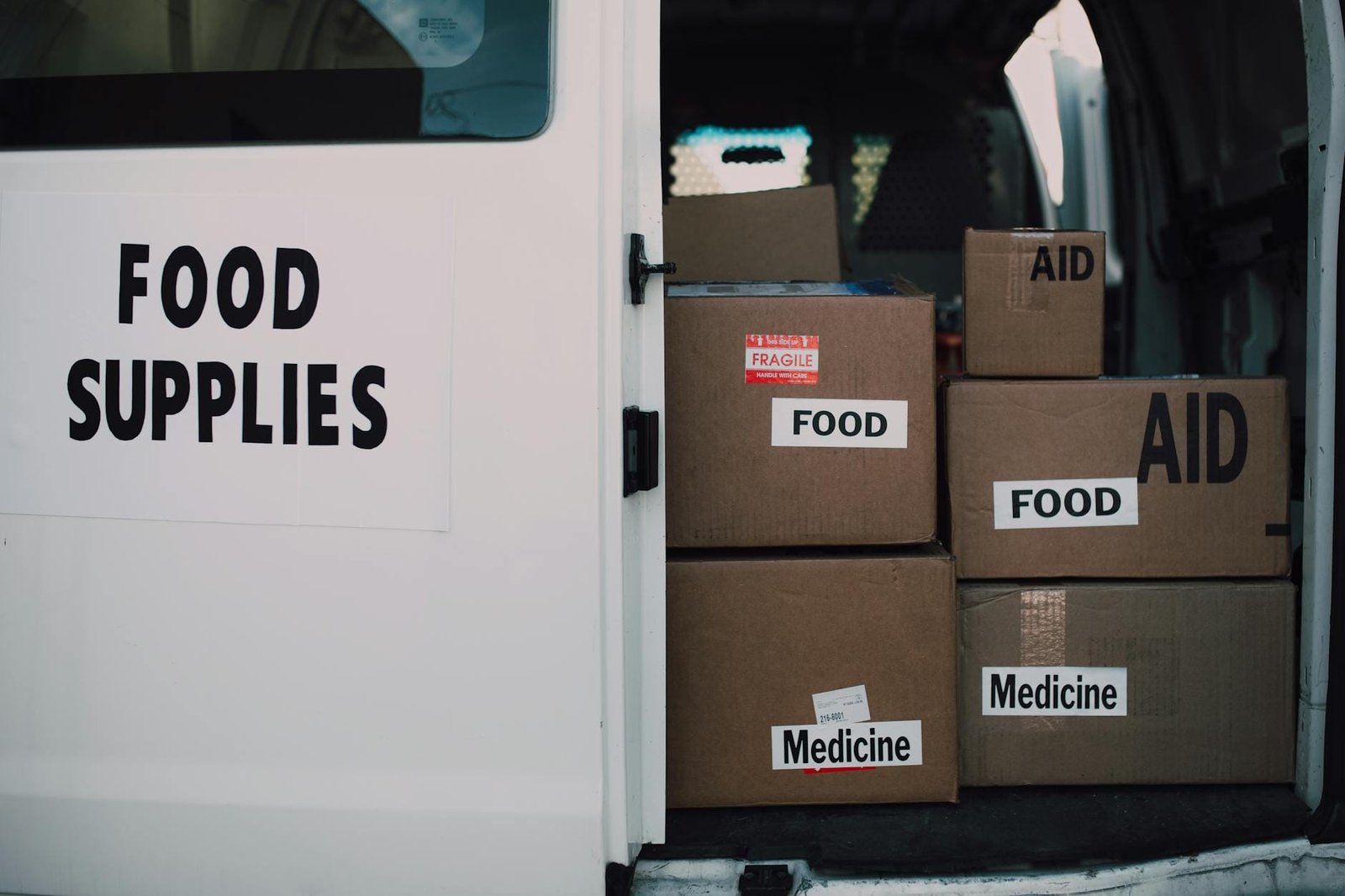 White van filled with cardboard boxes labeled food, aid, and medicine