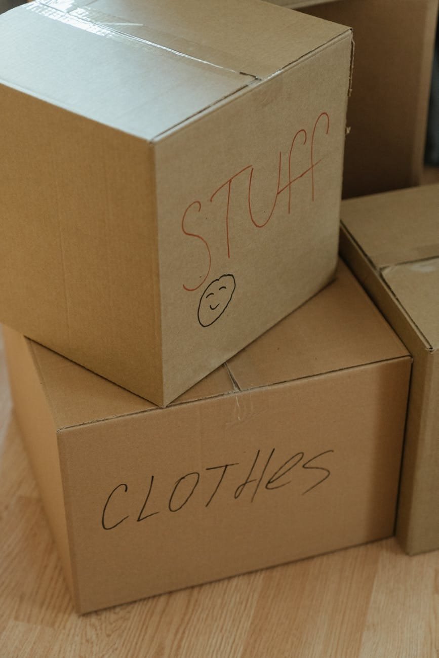 Stacked moving boxes labeled stuff and clothes on a wooden floor