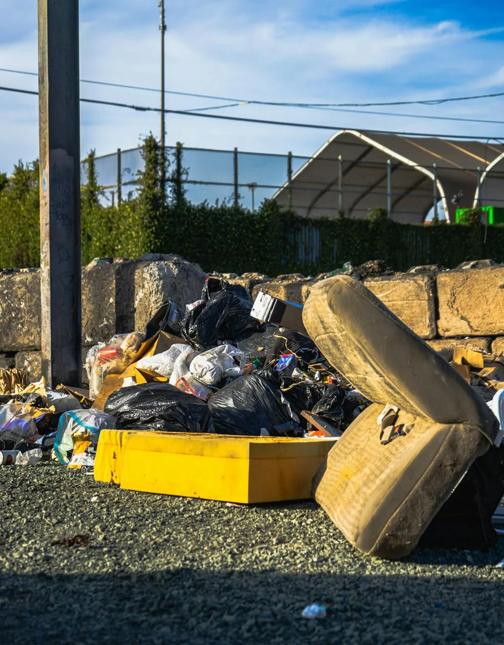 Large pile of discarded junk, trash bags, and debris on a gravel lot